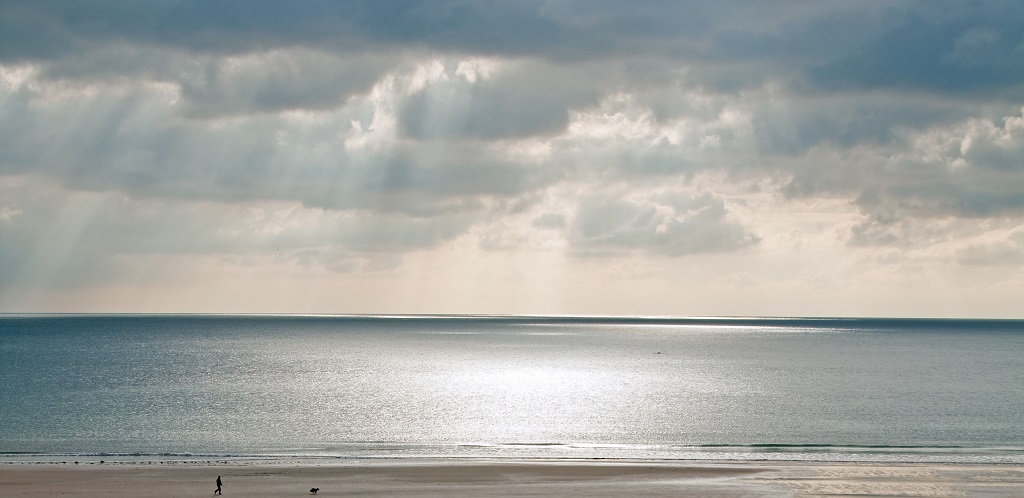 Screenshot of calm sea to the horizon with sunlight steaking through moody clouds